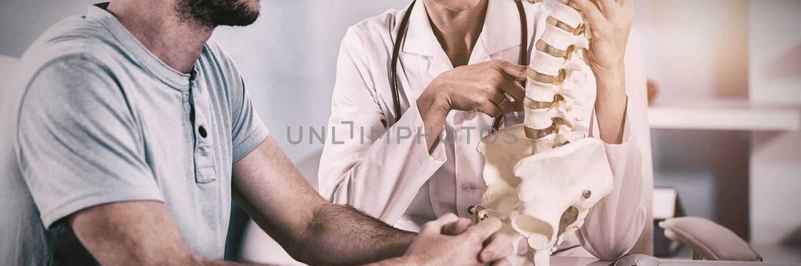 Physiotherapist explaining the spine model to patient by Wavebreakmedia