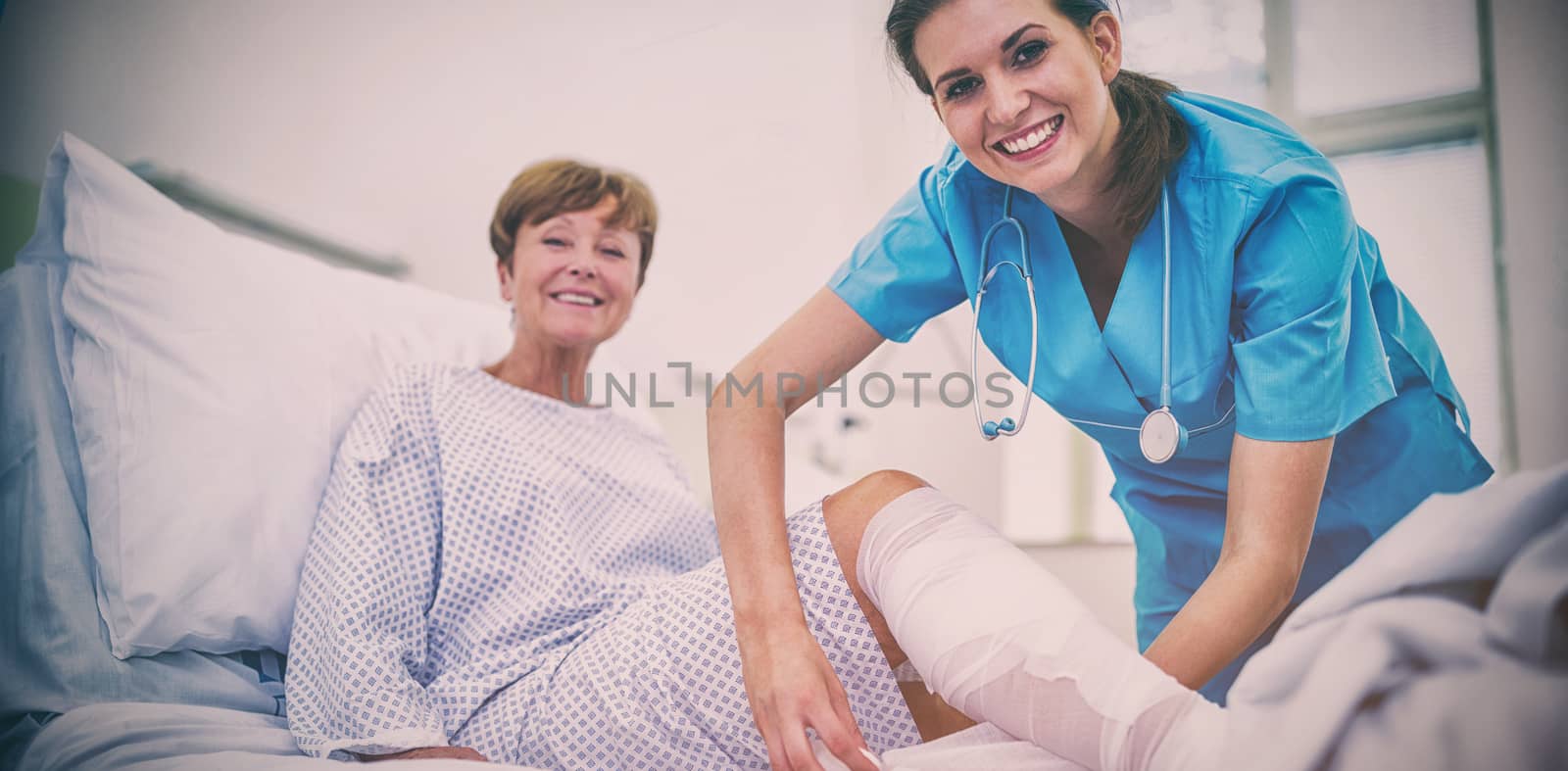 Portrait of smiling nurse bandaging leg of patient in hospital