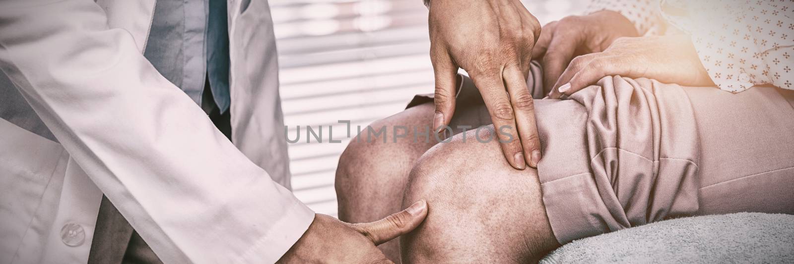 Mid section of doctor examining patient knee in clinic