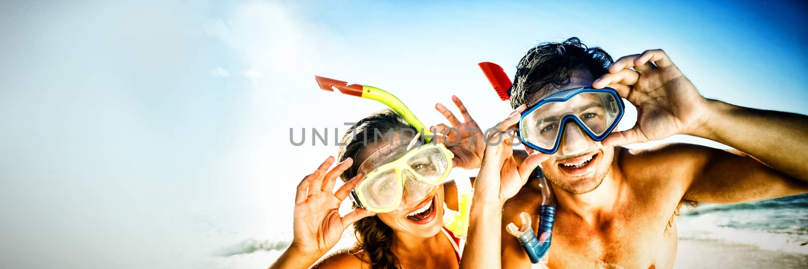 Portrait of happy young couple posing with diving mask on beach