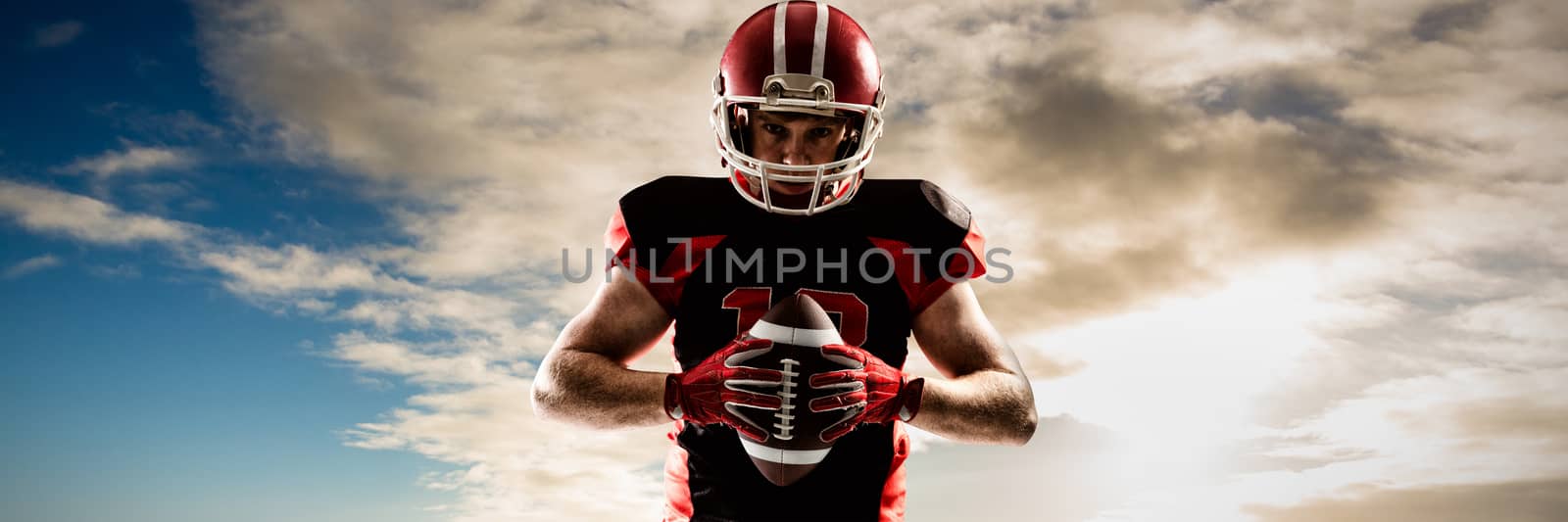 American football player standing with helmet and ball against cloudy sky over countryside