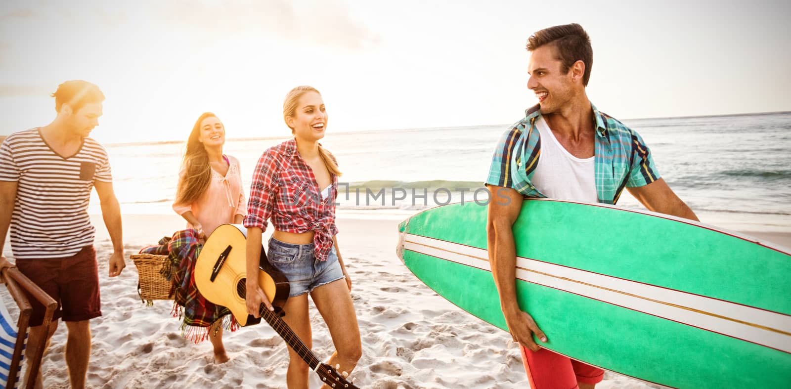 Friends carrying a surfboard and basket at the beach
