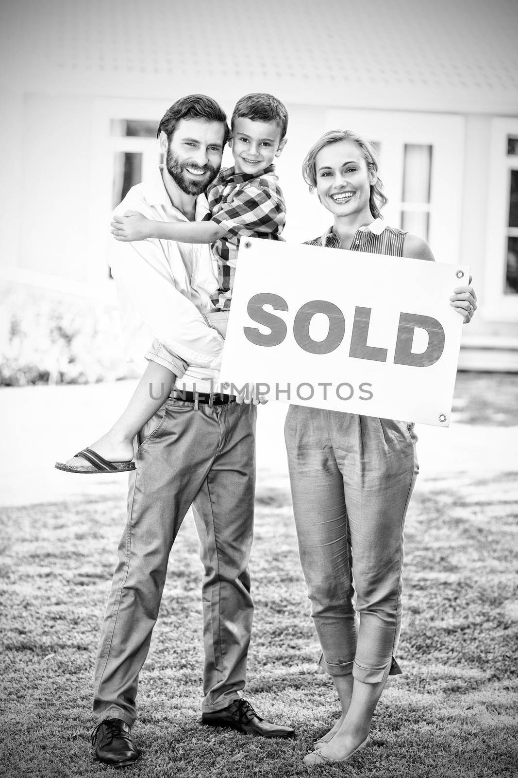 Portrait of happy family standing outside home with sold sign