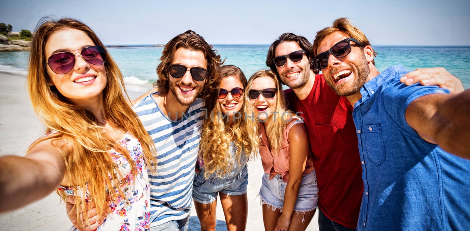 Cheerful friends standing on shore at beach during sunny day