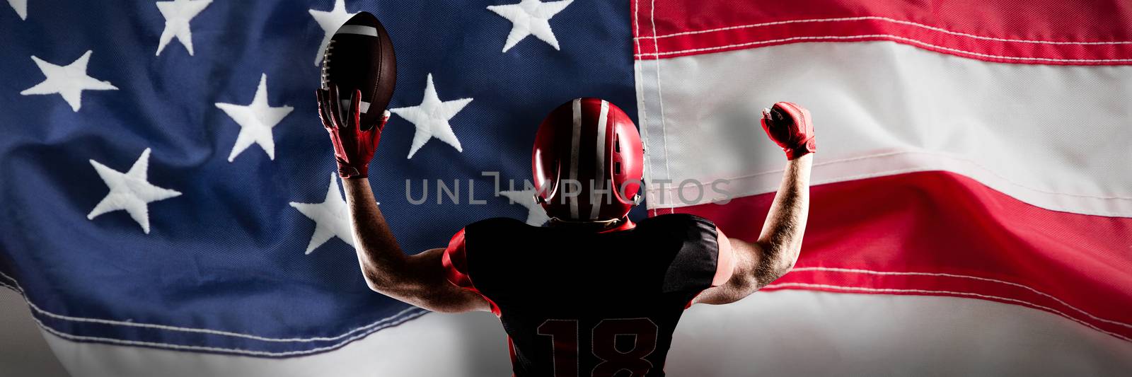 American football player standing with helmet holding football in victory against full frame of american flag