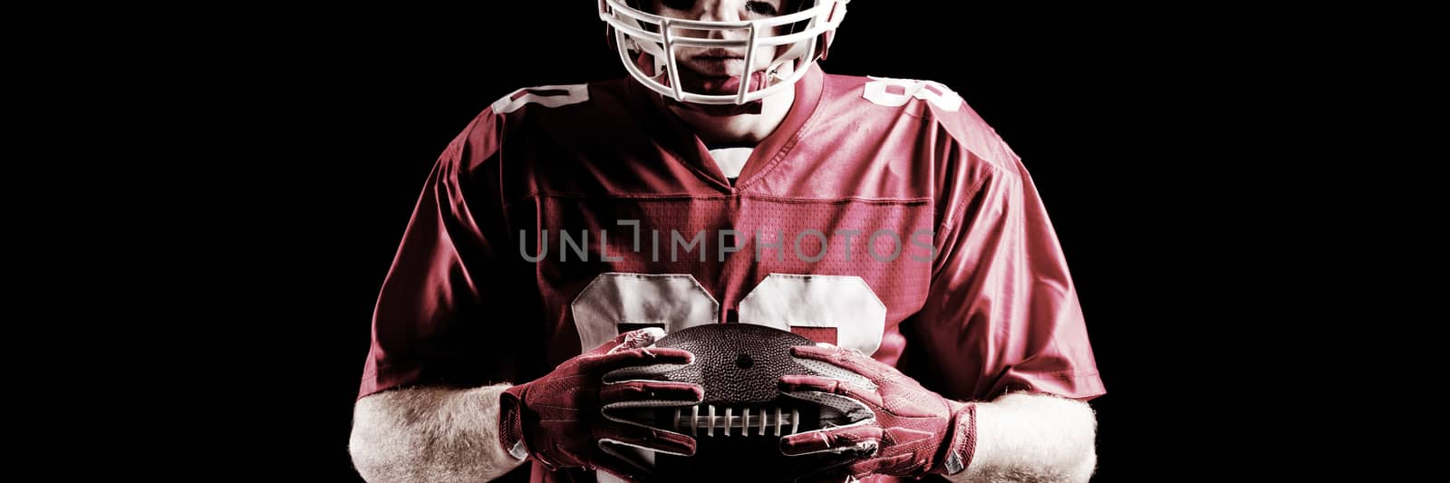 American football player holding rugby ball against black background