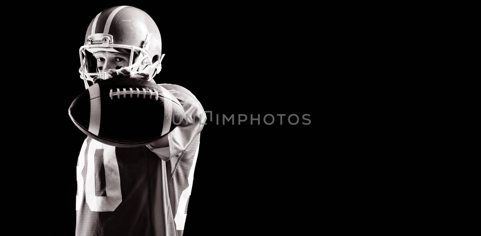 American football player standing with rugby ball and helmat against black background