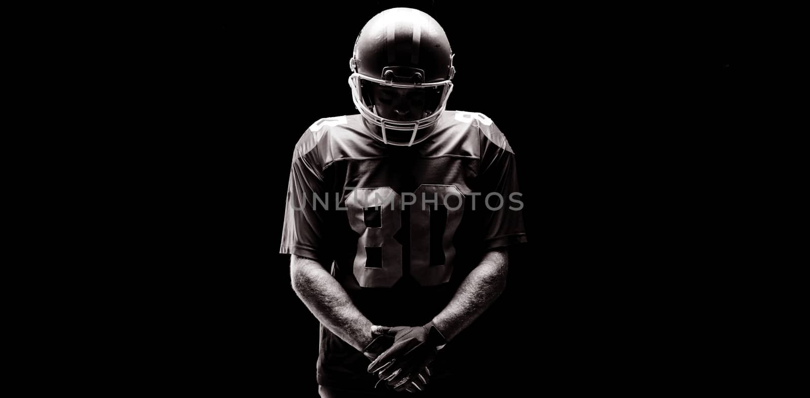 American football player standing with rugby helmat against black background
