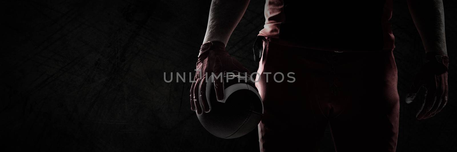 American football player standing with rugby ball against panoramic shot of grunged concrete wall