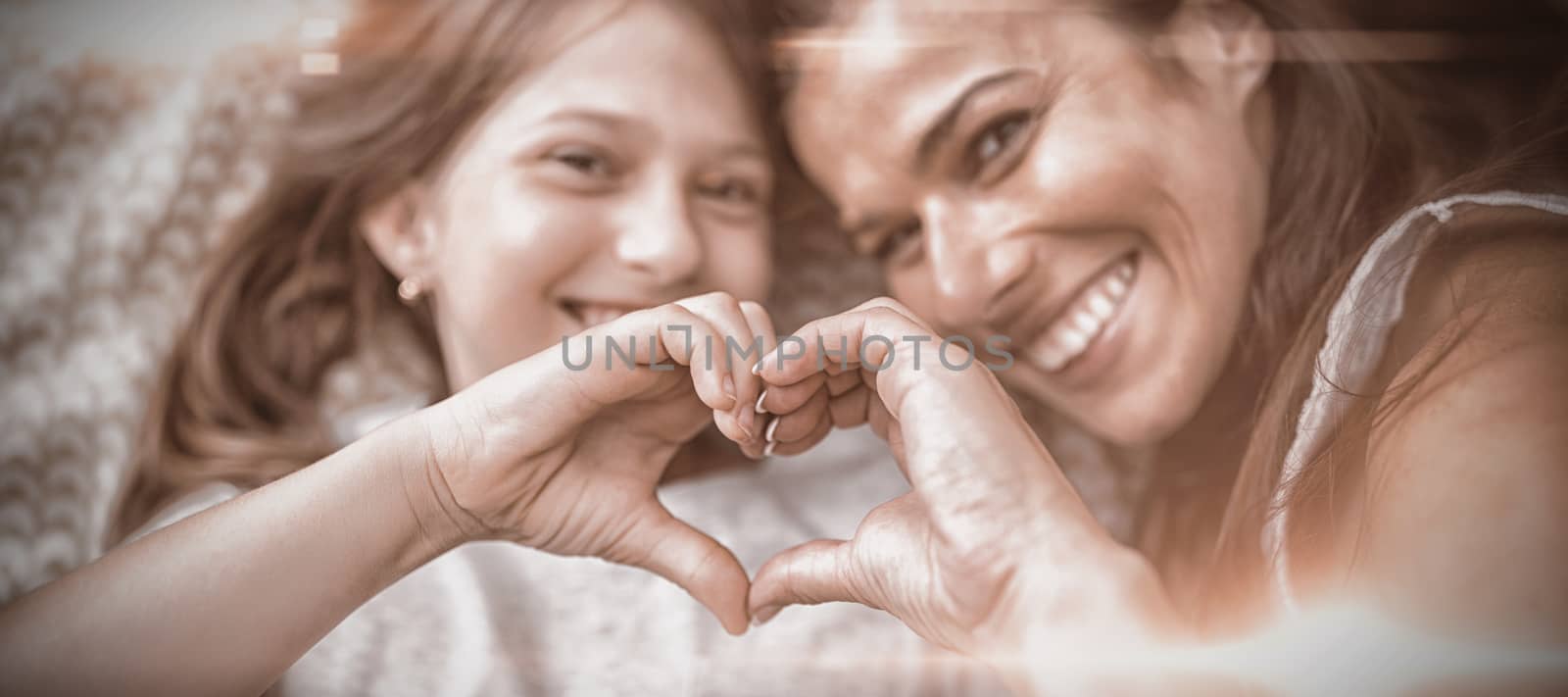 Mother and daughter making heart shape with hands while lying on bed at home