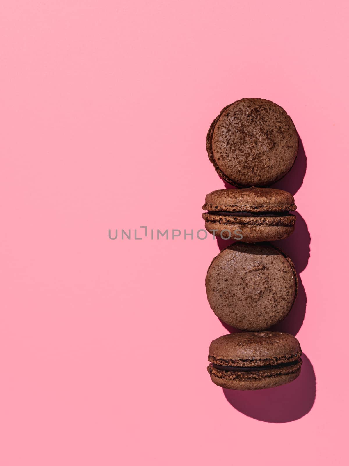 Chocolate macarons with copy space. Row of perfect french macarons or macaroons on pink background. Top view or flat lay. Hard light