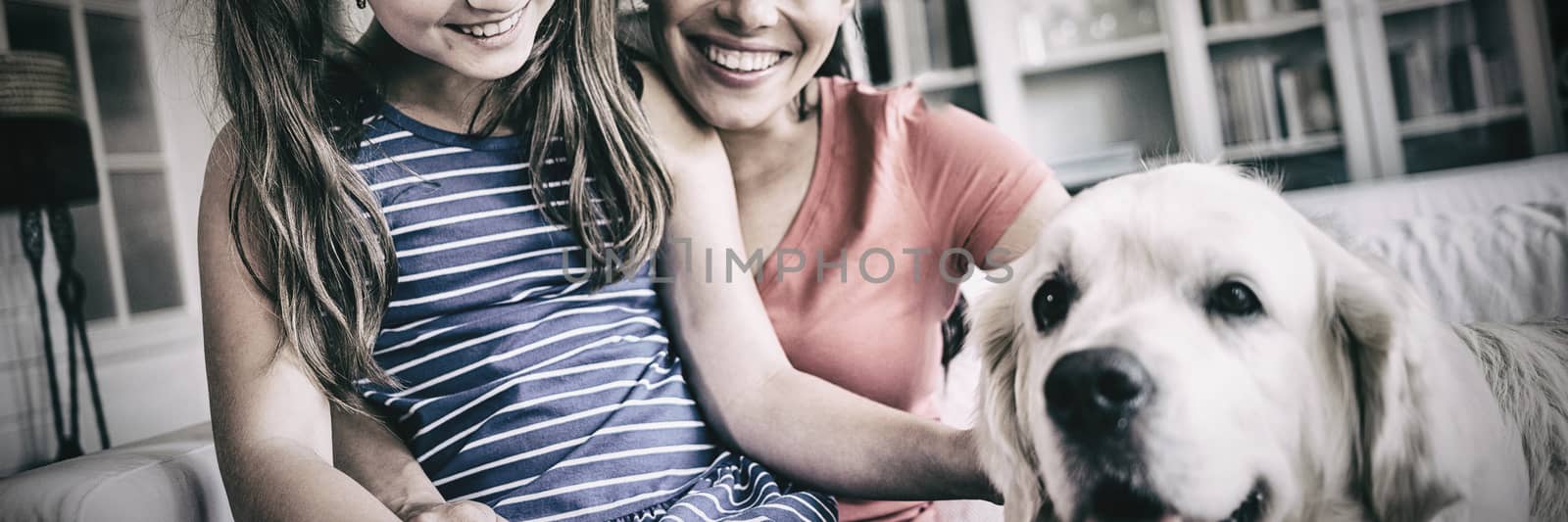 Mother and daughter sitting with dog in living room by Wavebreakmedia