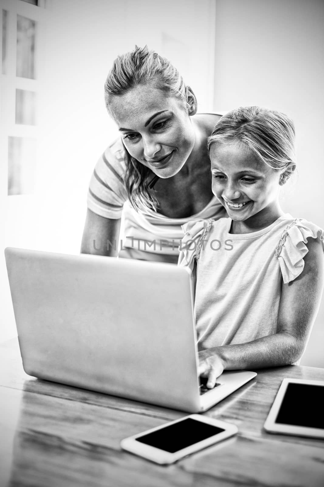 Mother assisting daughter in uising laptop at home  by Wavebreakmedia