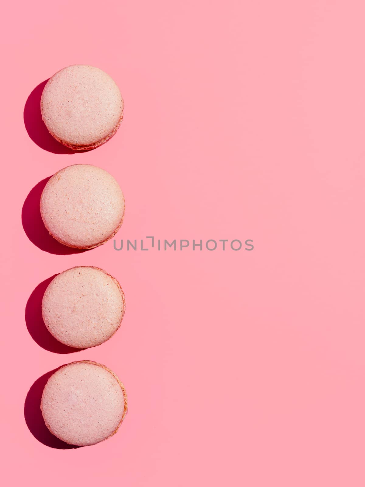 Pink macarons with copy space. Row of perfect french macarons or macaroons on pink background. Top view or flat lay. Hard light