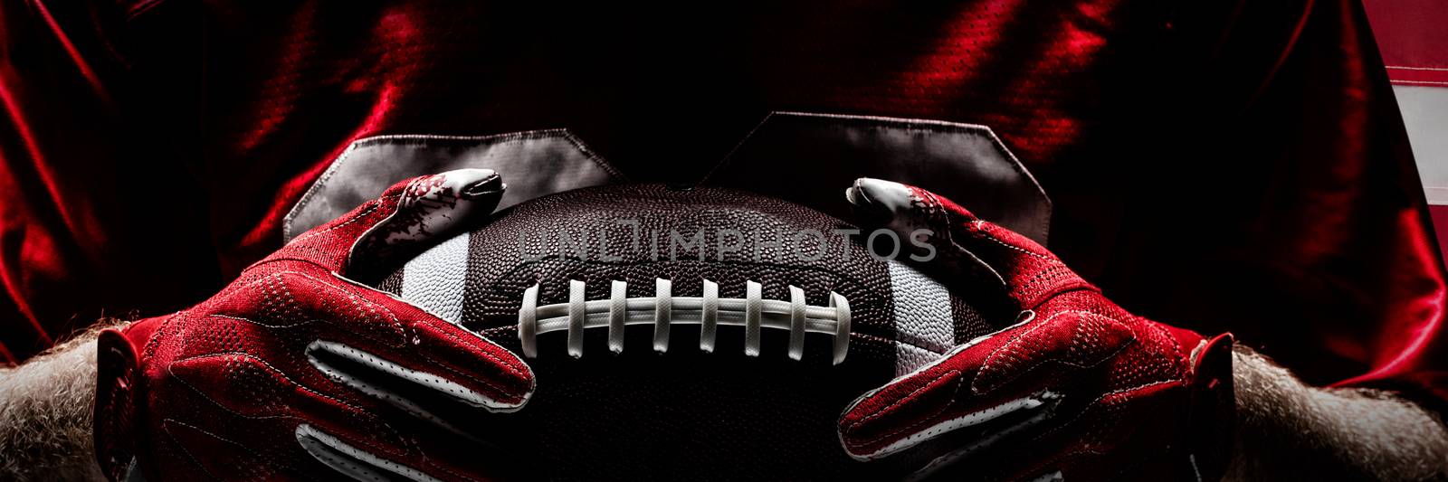 American football player standing with rugby helmet and ball against close-up of an american flag