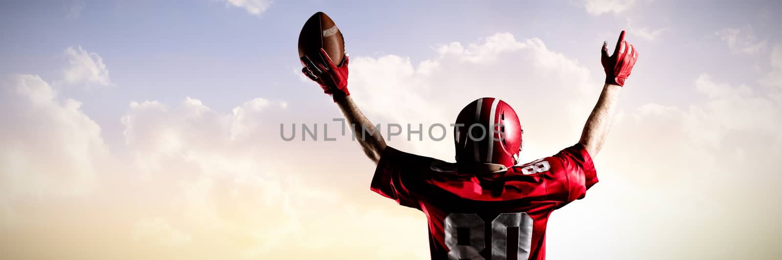 American football player in helmet holding rugby ball against sunset with clouds