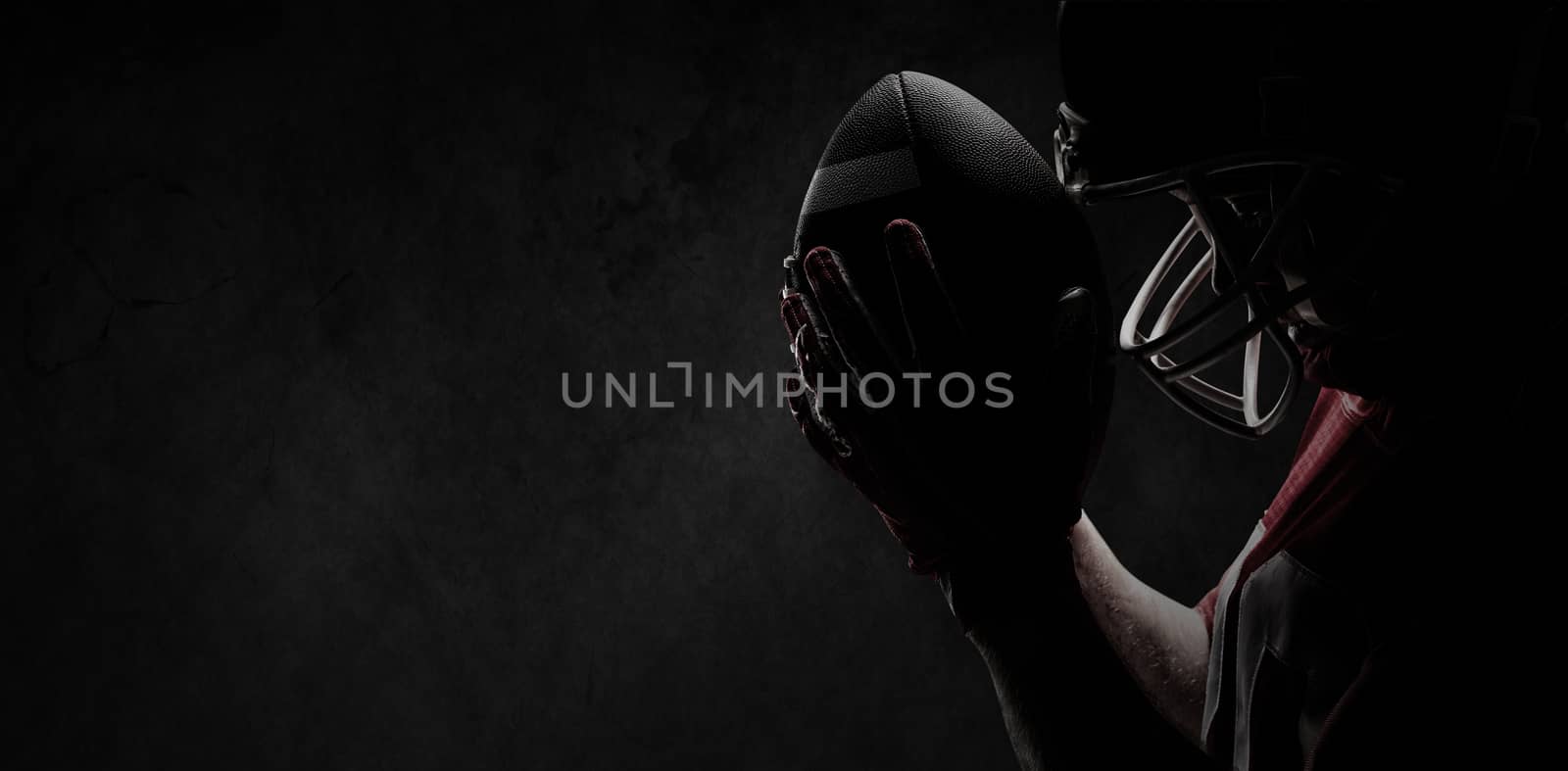 American football player standing with rugby helmet and ball against full frame shot of concrete wall