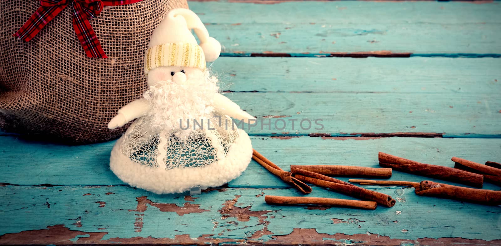 Cinnamon sticks and christmas decoration by sack on wooden table against white background with vignette