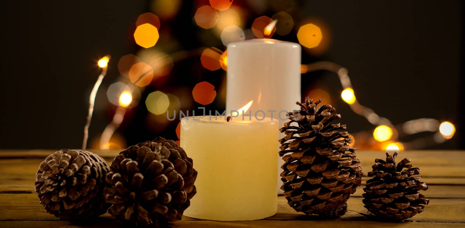 Close up of pine cones with illuminated candles on table against christmas balls against unfocused tree