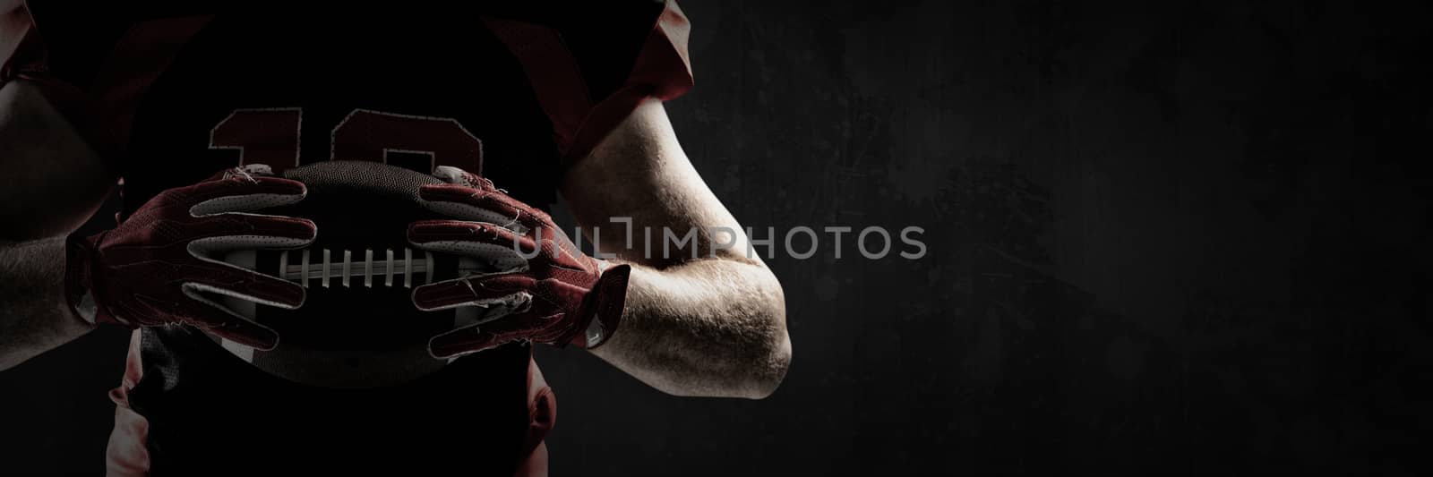 American football player holding rugby ball against full frame shot of grunged concrete wall