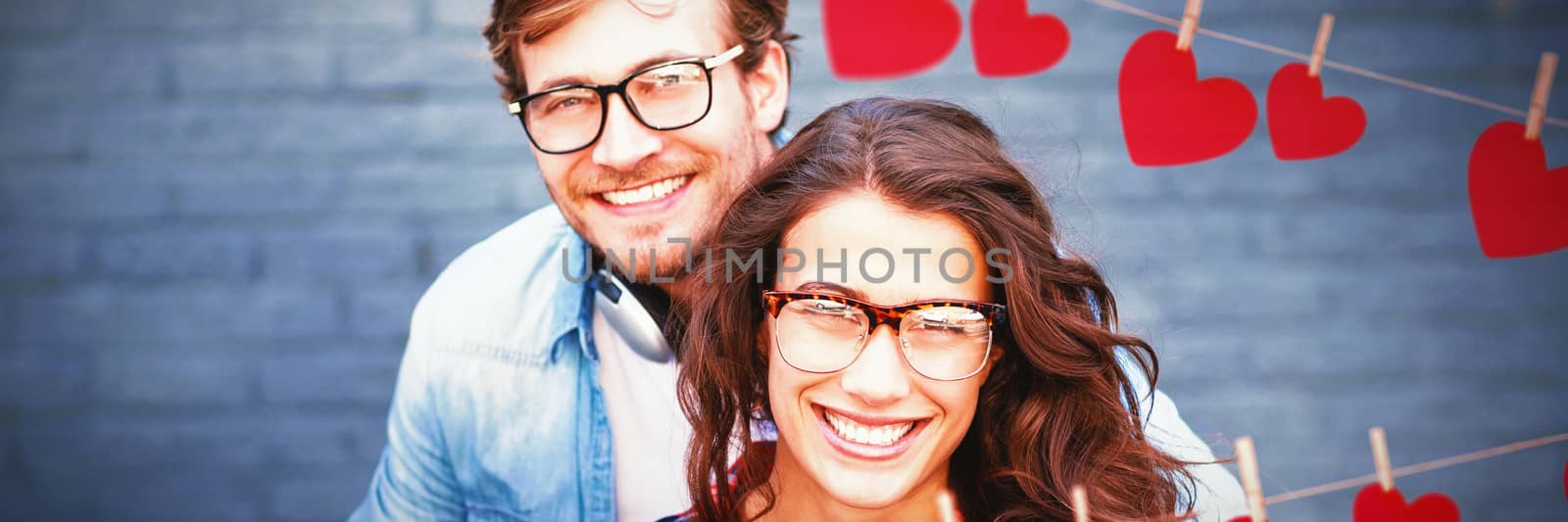 Hearts hanging on a line against portrait of happy young couple in spectacles