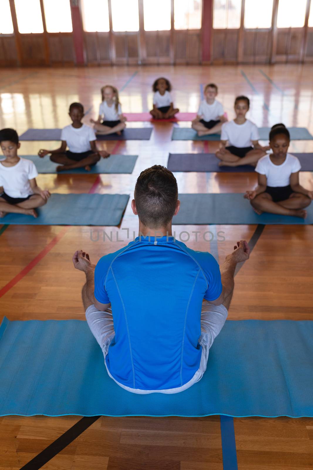 High angle view of yoga teacher teaching yoga to school kids in school