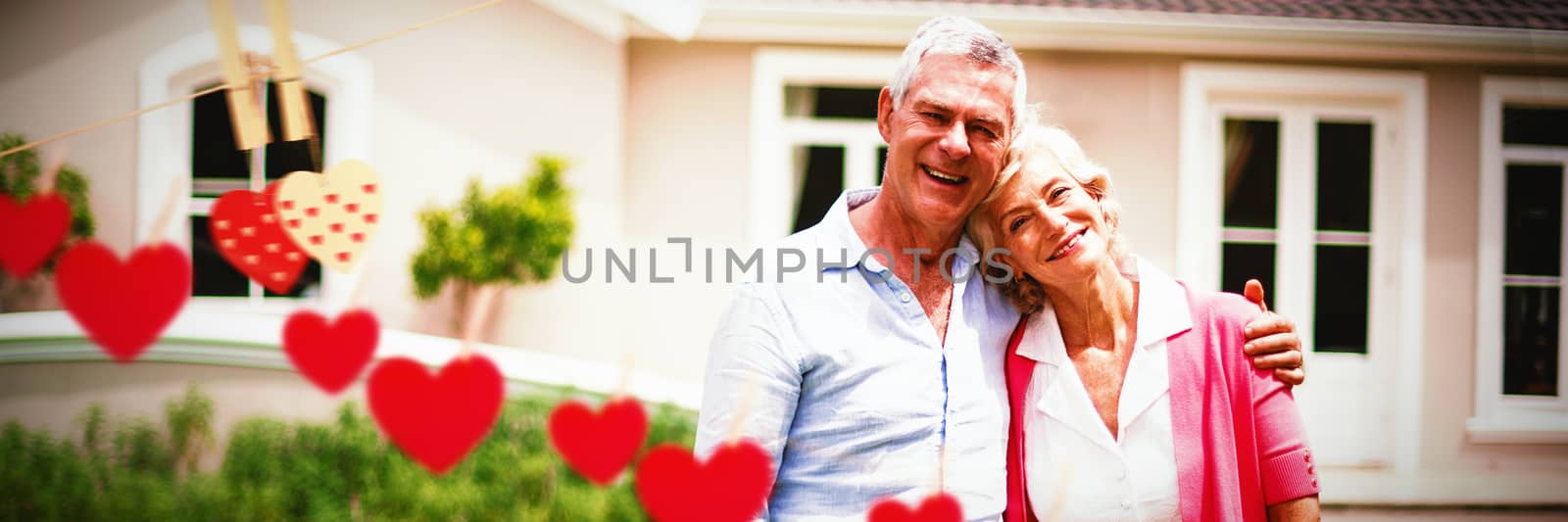 Hearts hanging on a line against senior couple with arms around standing in yard 