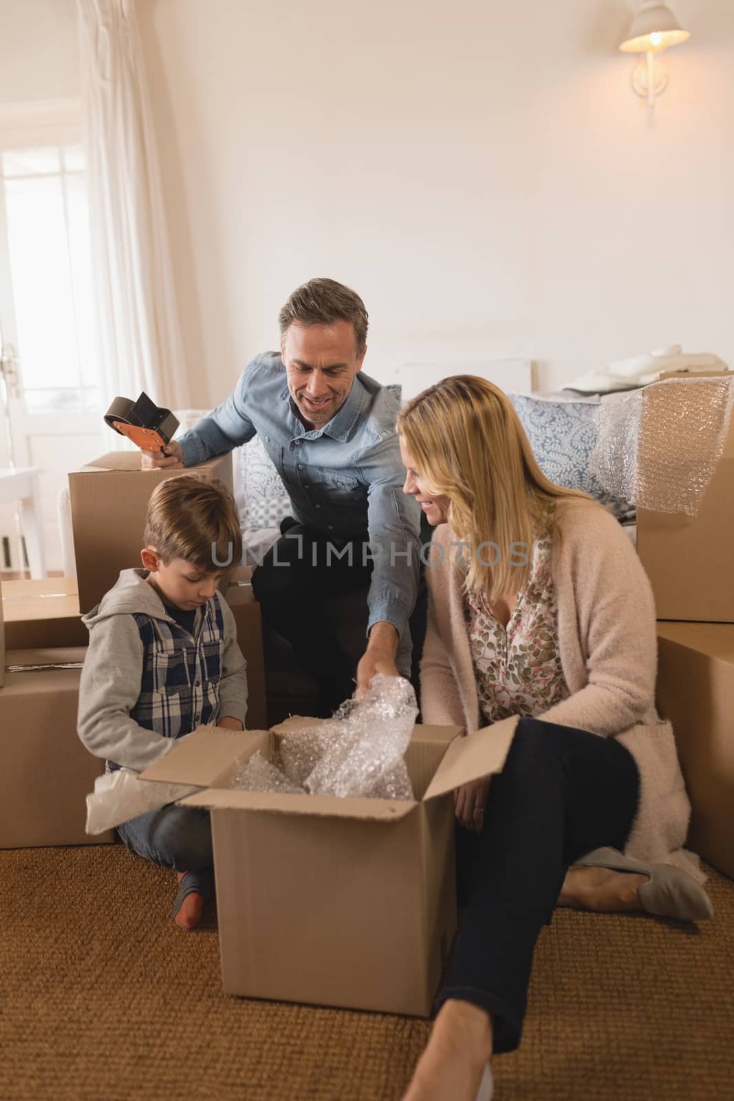 Front view of happy family in casual clothes unpacking cardboard boxes in their new home