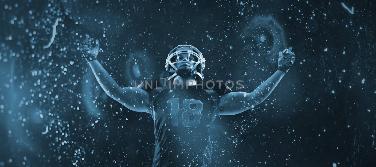 American football player standing with arms up against old weathered wall