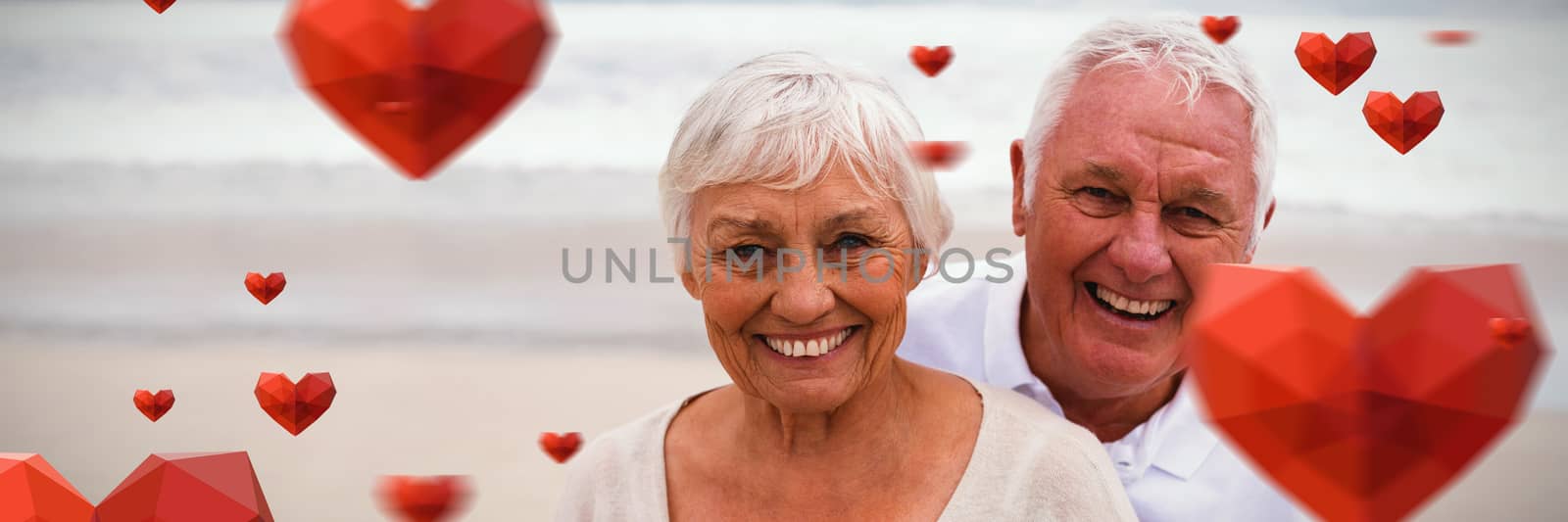 Red heart with white blackground against portrait of senior couple standing on the beach