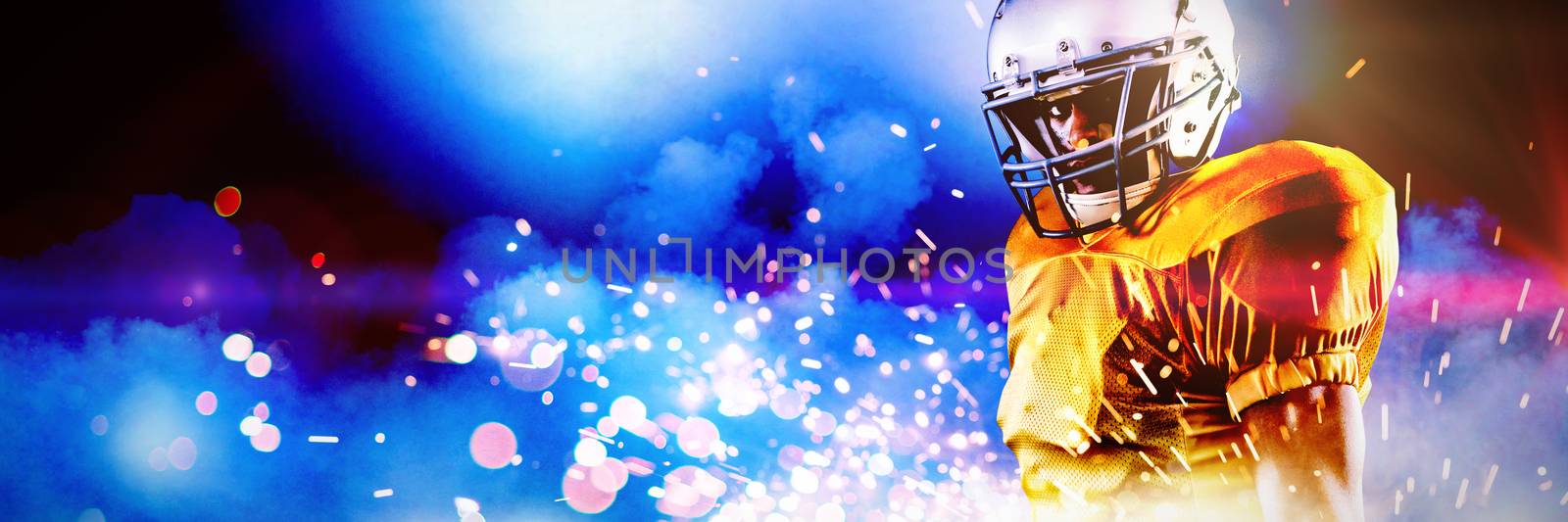 Portrait of confident American football player in helmet holding ball against firework bursting sparkle background