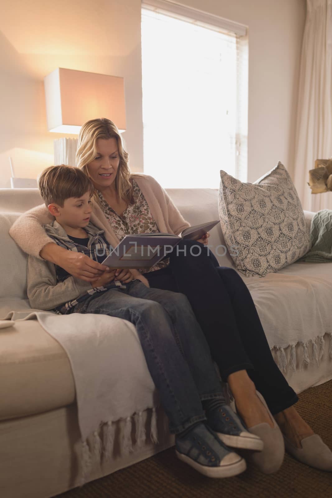 Side view of attractive mother with her son spending time together while reading story book in living room at home