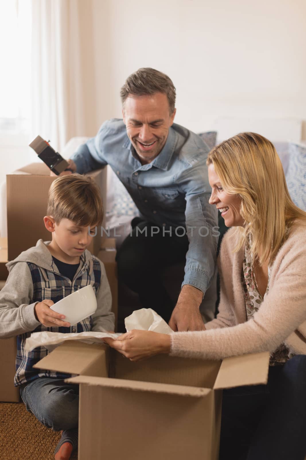 Side view of happy family spending time together while unpacking cardboard boxes in their new home