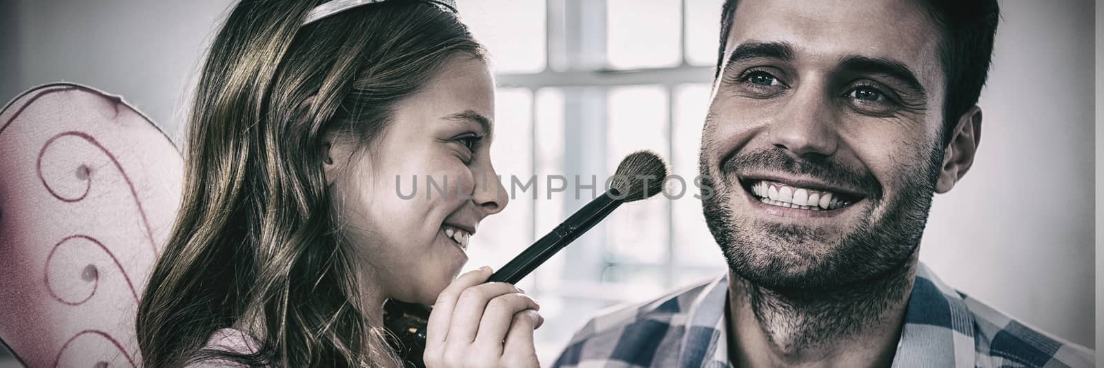Girl dressed up in a fairy costume applying make-up on fathers face by Wavebreakmedia