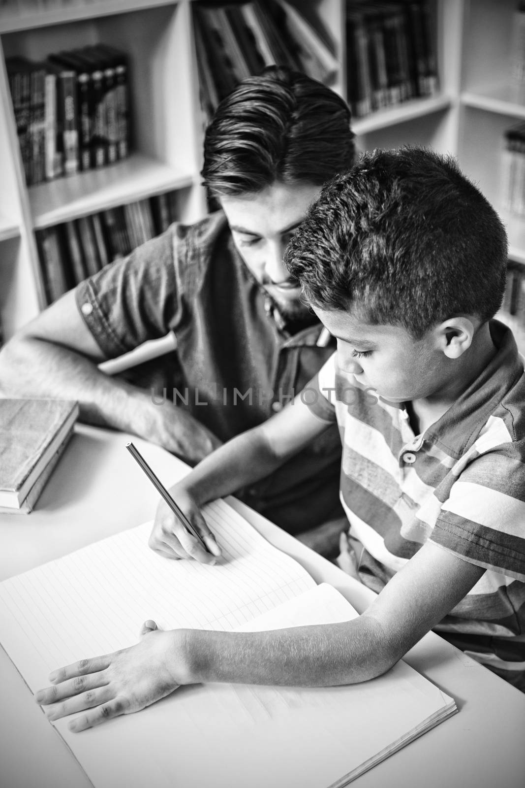Teacher helping school kid with his homework in library at school