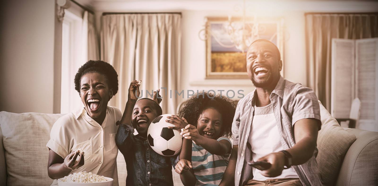 Parents and kids having fun while watching television in living room at home