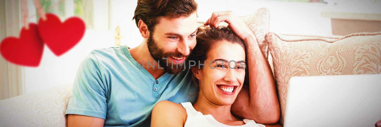 Hearts hanging on a line against couple sitting on sofa and using laptop