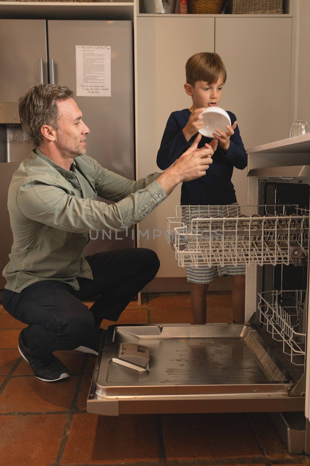 Side view of father and son placing bowl in dishwasher in the kitchen at home