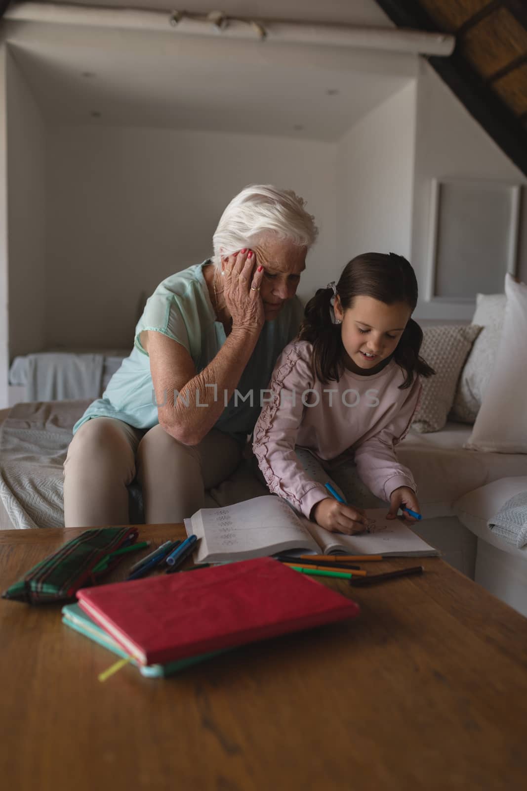 Front view of a grandmother helping her granddaughter with homework in living room at home