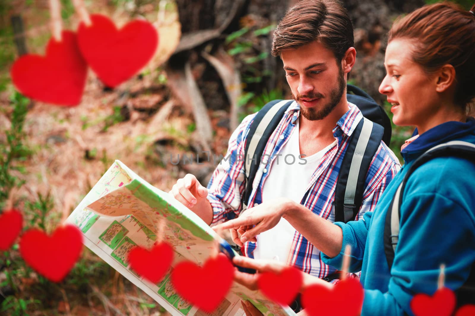 Hearts hanging on a line against couple discussing over map in forest