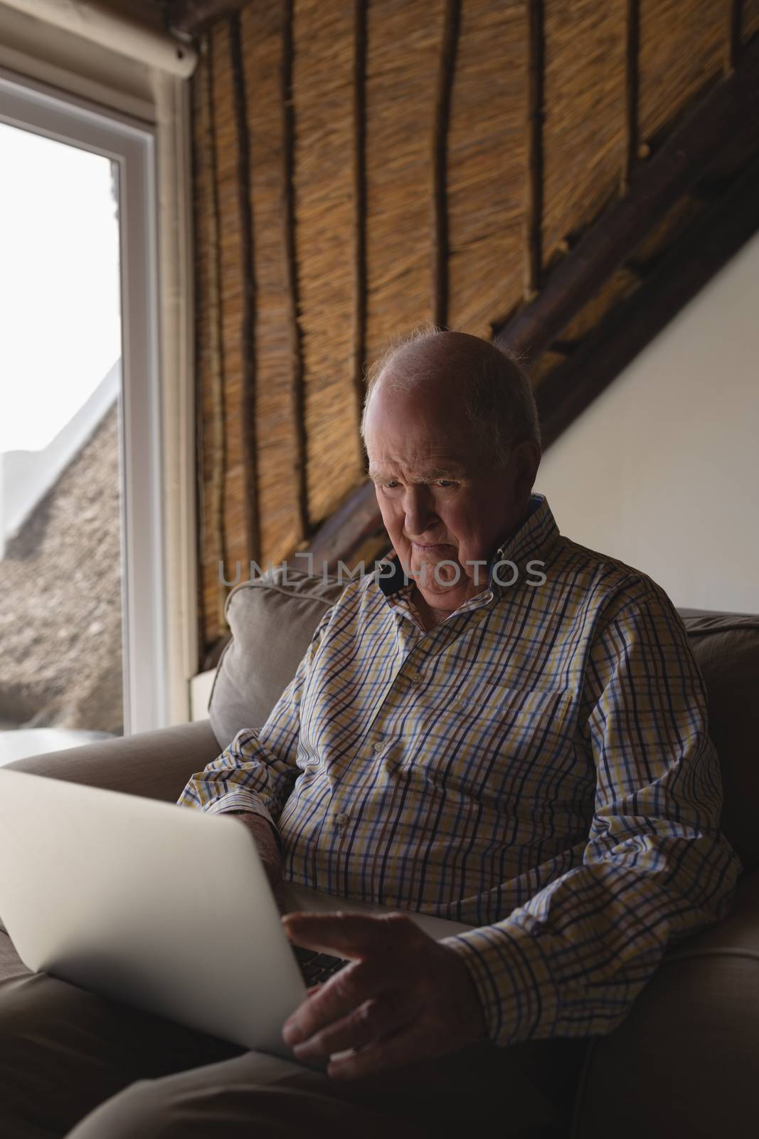 Side view of a senior man using laptop while sitting on a sofa in living room at home