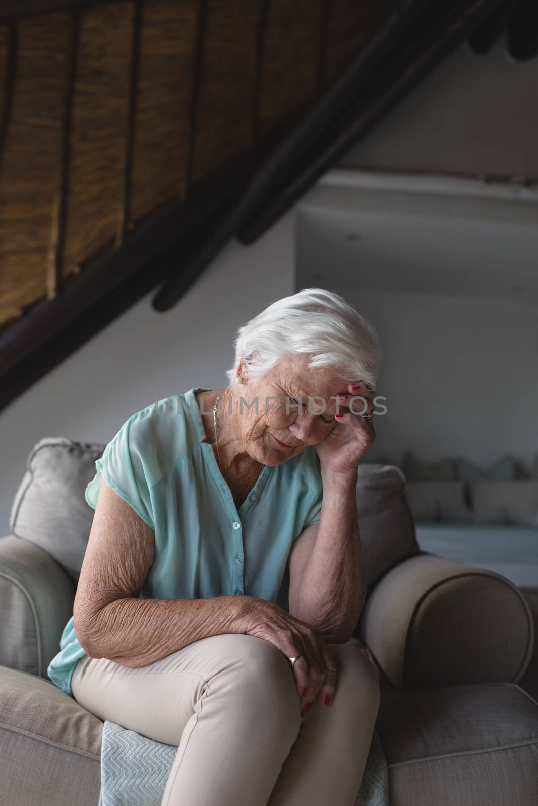 Front view of a worried senior woman sitting on sofa and holding her head in living room at home