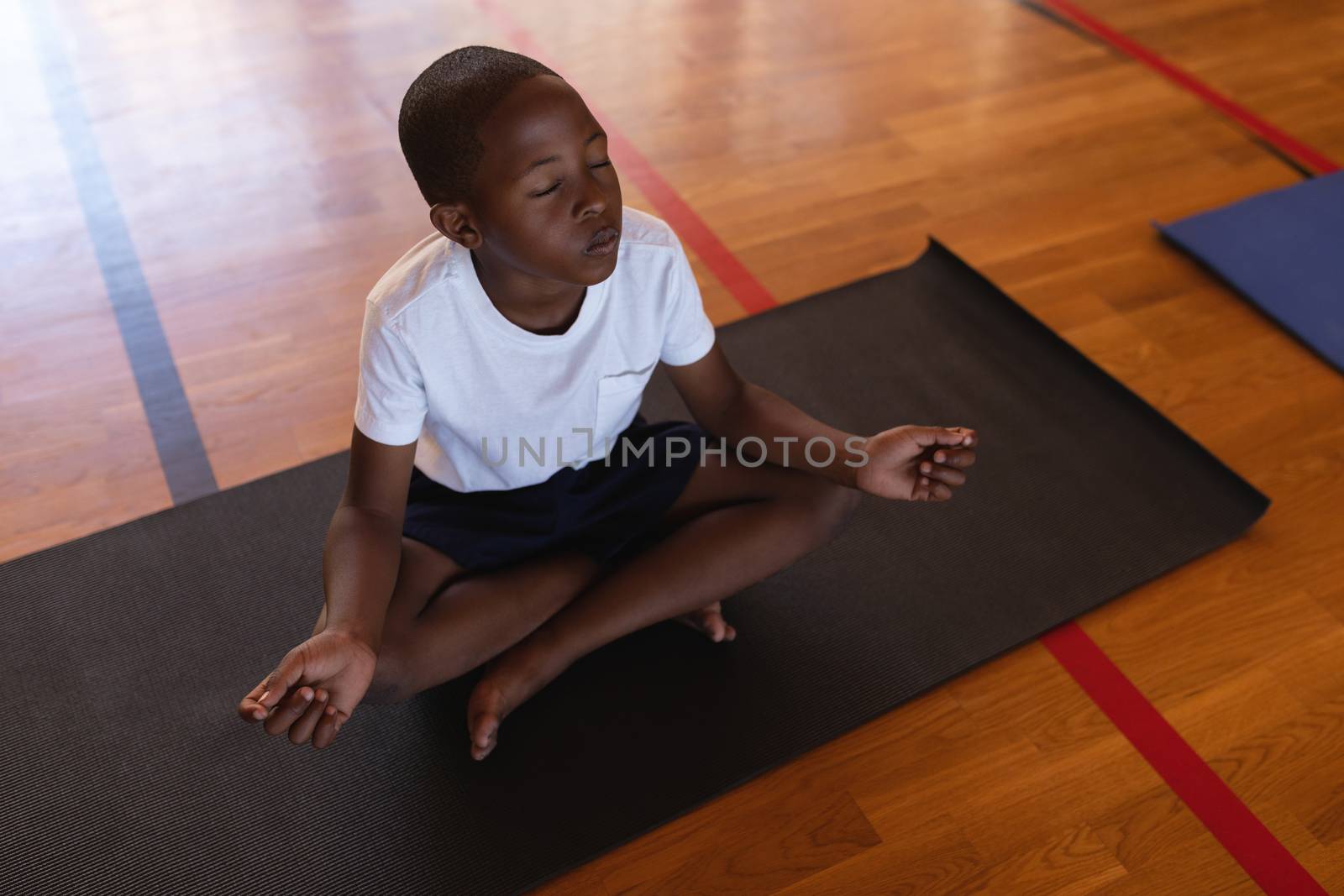 Schoolboy doing yoga and meditating on a yoga mat in school by Wavebreakmedia