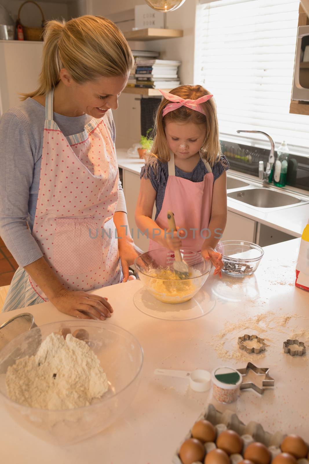 Front view of happy mother with her daughter baking cookies in kitchen at home