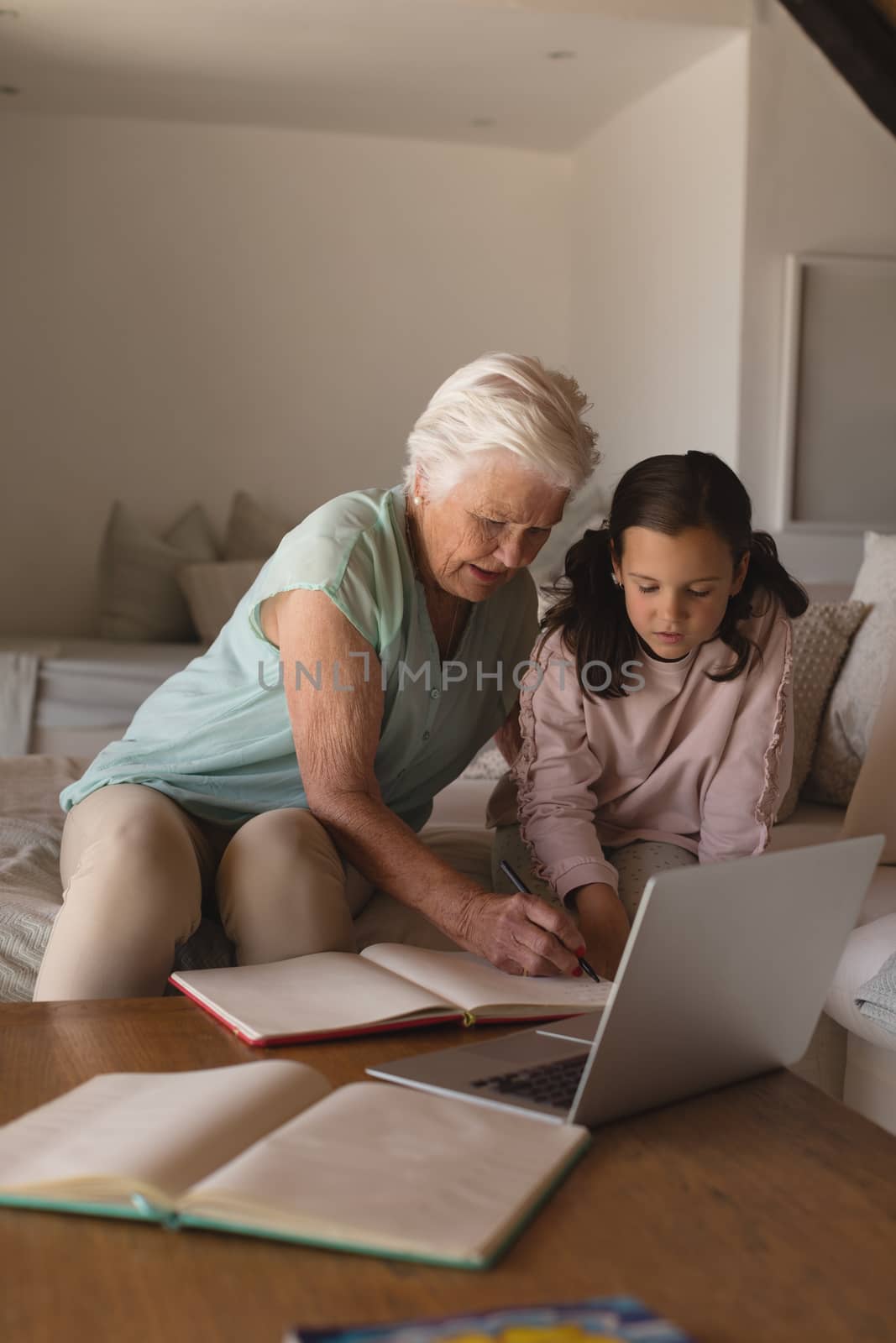 Front view of a grandmother helping her granddaughter with homework in living room at home