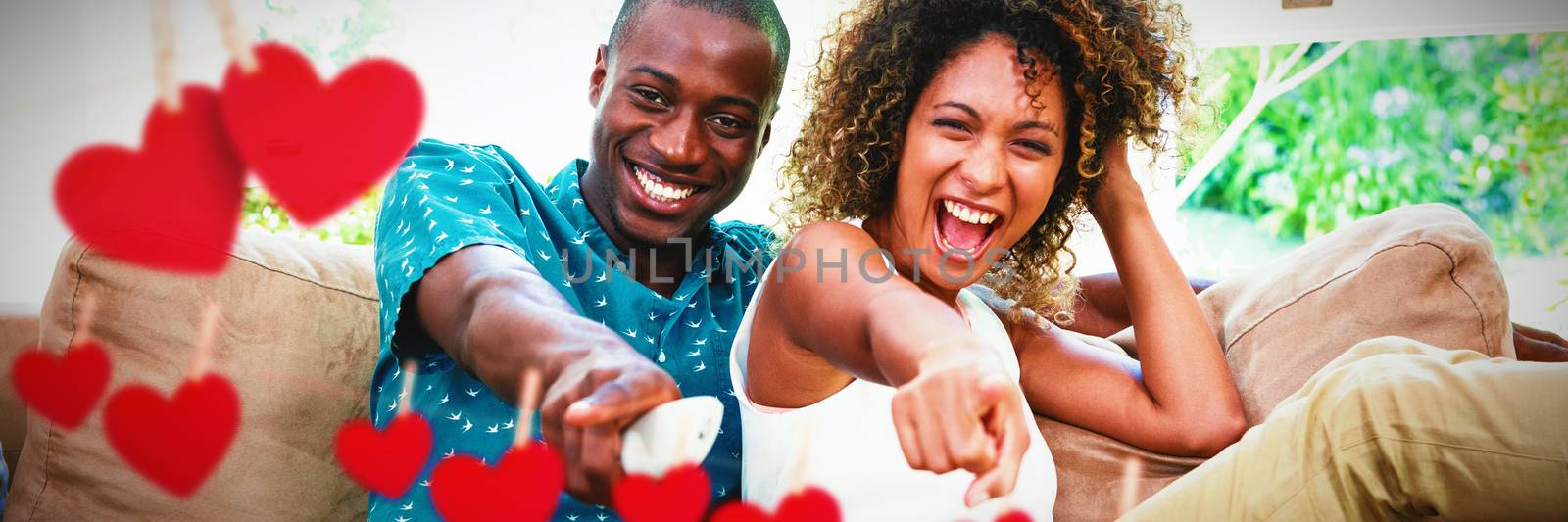 Hearts hanging on a line against happy young couple watching television