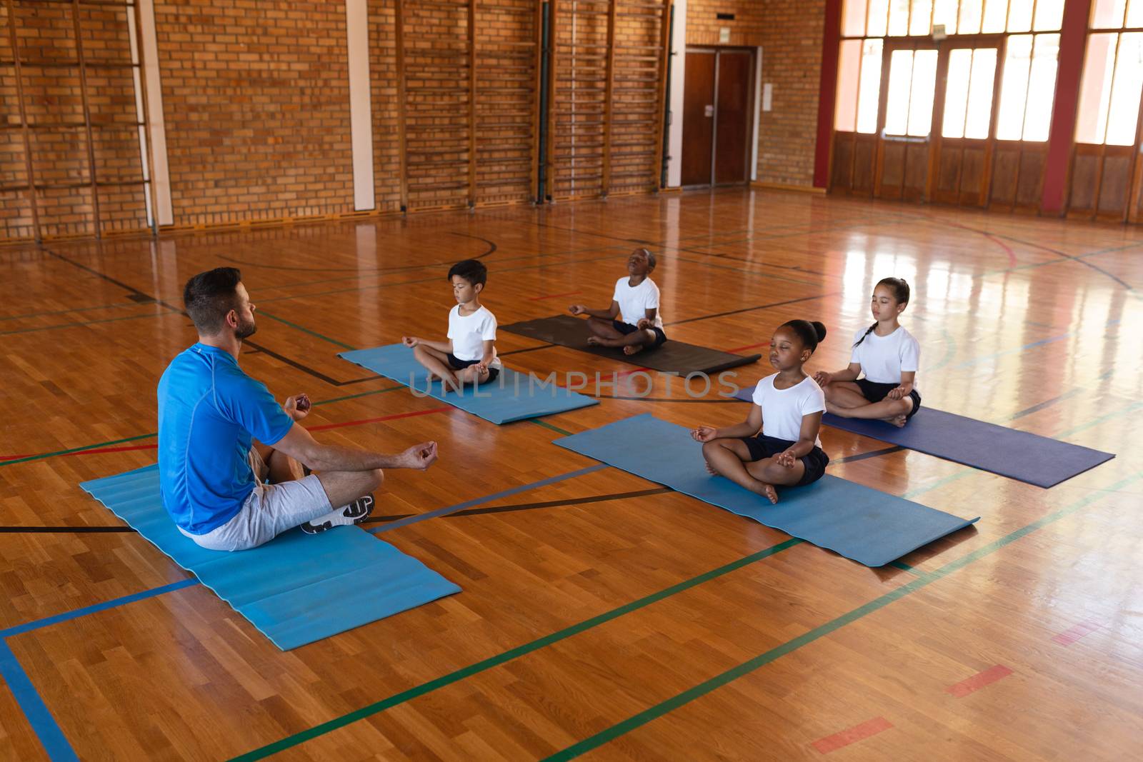 Side view of yoga teacher teaching yoga to school kids in school gymnast