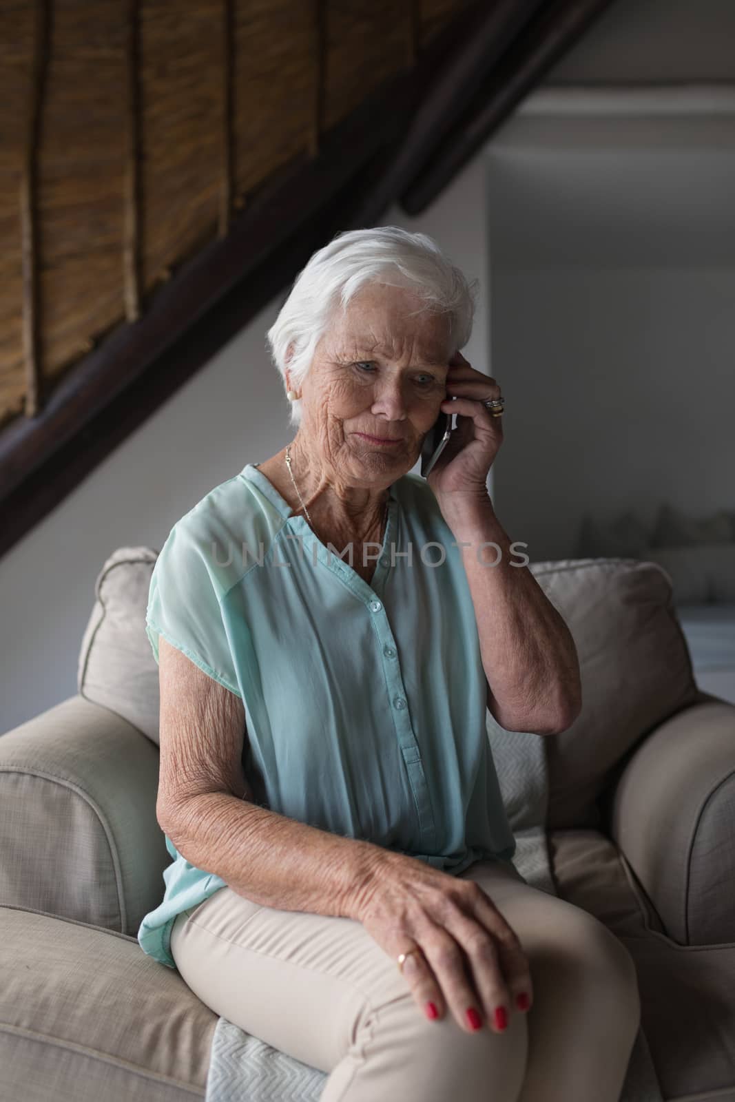 Front view of a senior woman talking on mobile phone while sitting on a sofa in living room at home