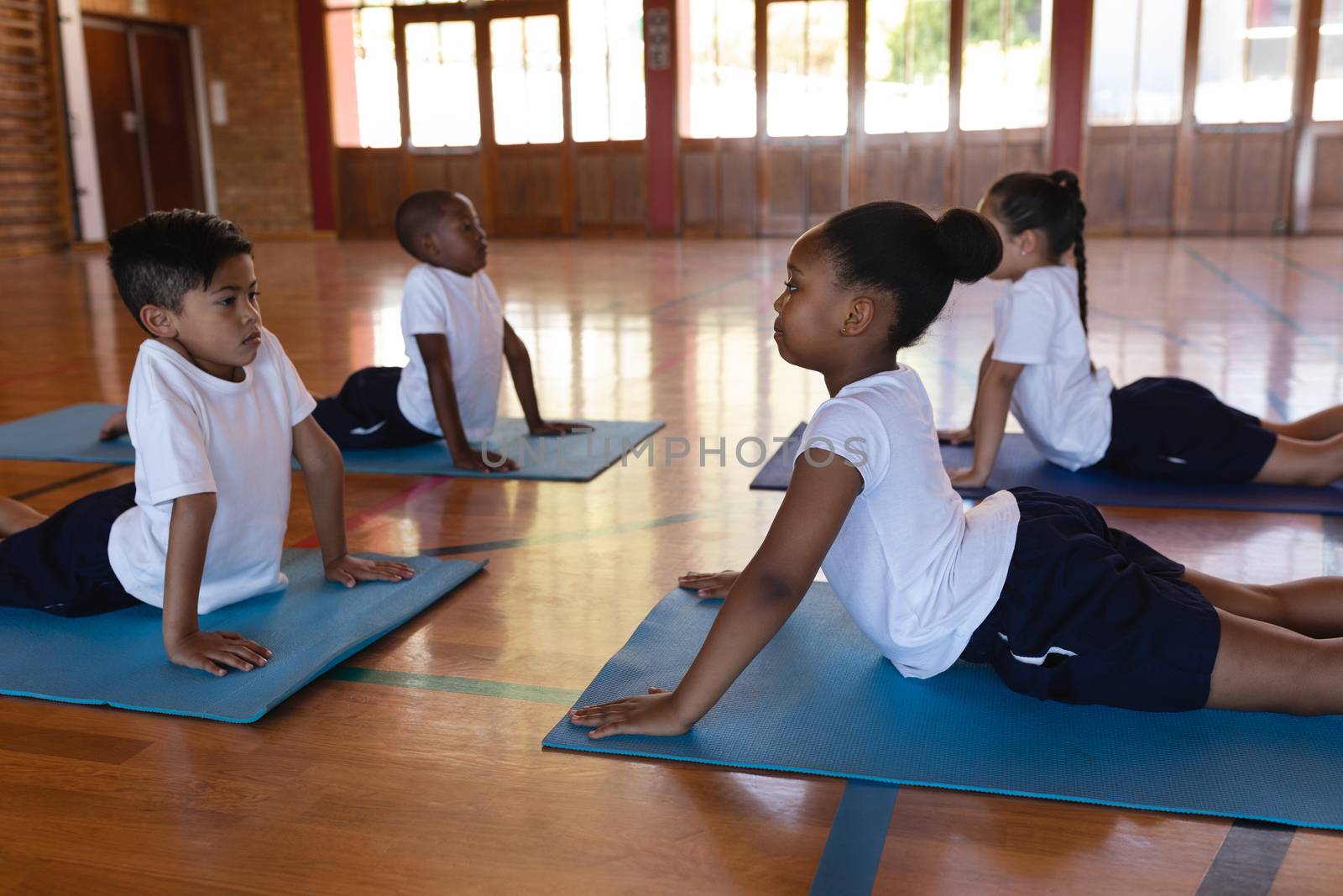 Side view of concentrate schoolkids doing yoga position on a yoga mat in school