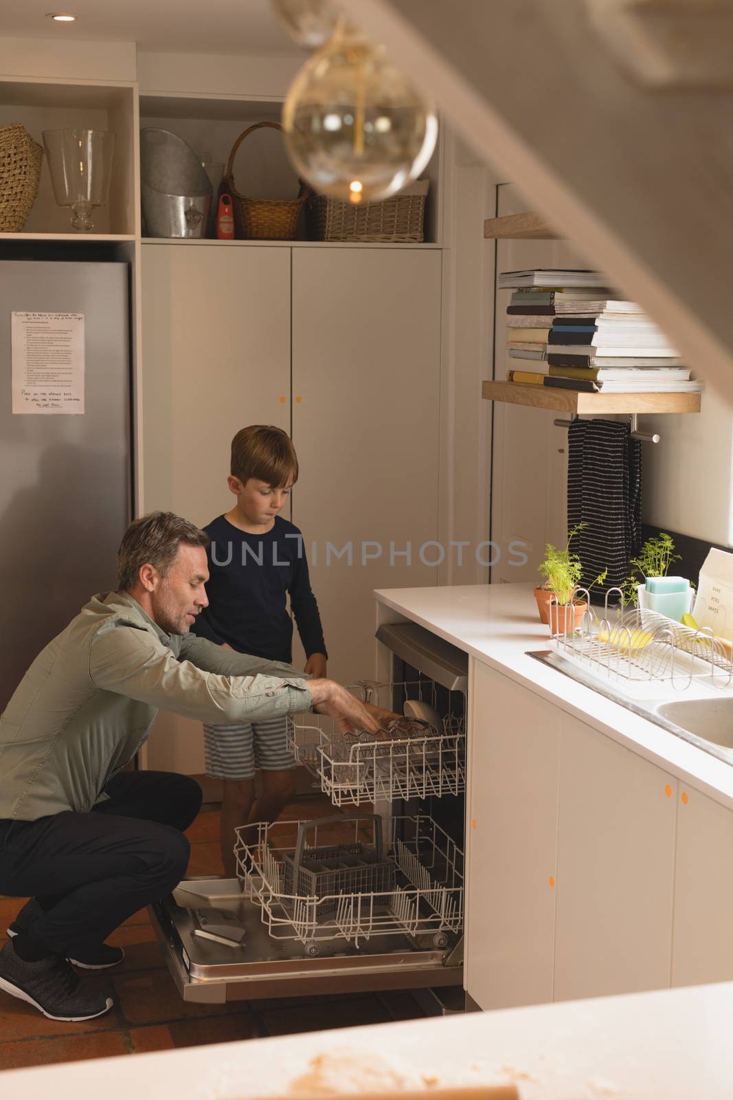 Side view of father and son putting utensils in dishwasher at home